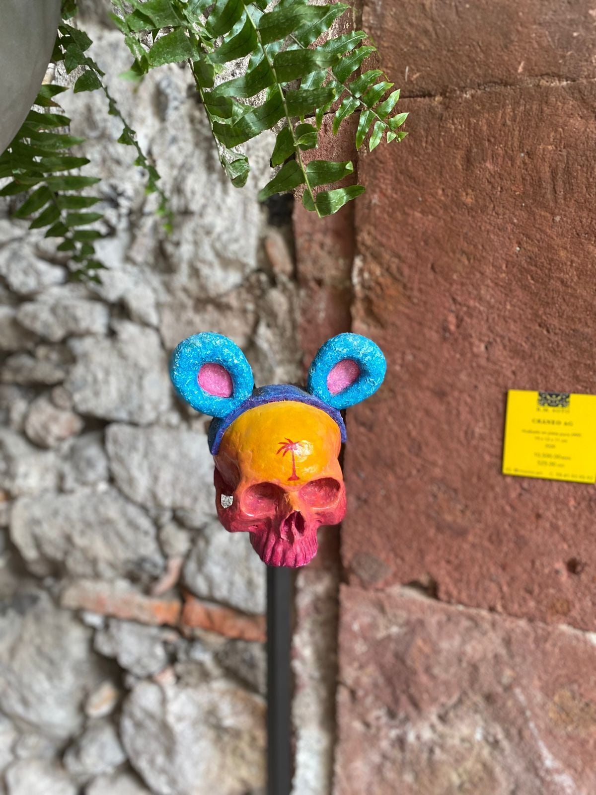 A decorative skull with a bear face, blue ears, and a pink nose, mounted on a pole.