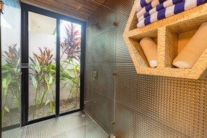 A room with a sliding glass door leading to a garden, a textured wall, and a wooden shelf with towels.