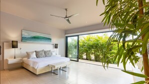Quarto moderno com uma cama grande, um ventilador de teto e vista para vegetação exuberante através de amplas janelas.