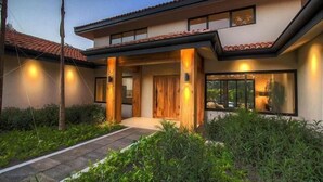 Uma casa moderna de dois andares com telhado de telhas, varanda frontal e entrada bem iluminada.