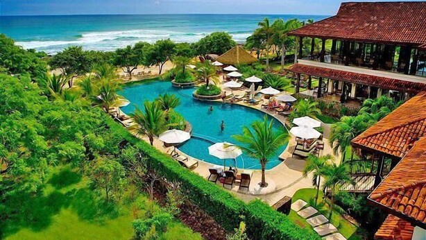 Um resort com uma piscina grande, palmeiras e vista para o oceano.