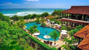 Um resort com uma piscina grande, palmeiras e vista para o oceano.