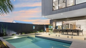 Un espace piscine extérieur moderne, doté d’une structure en verre, d’un coin repas avec mobilier d’extérieur et offrant une vue sur le ciel.