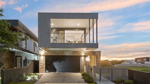 Une maison moderne à deux étages, dotée d’un garage, d’une façade en pierre et d’un balcon aménagé avec des sièges.