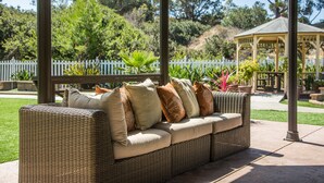 A wicker sofa with cushions, a gazebo, and a white picket fence in a garden setting. - 1 Bedroom/1 Bathroom Sleep 4 SC (San Clemente)