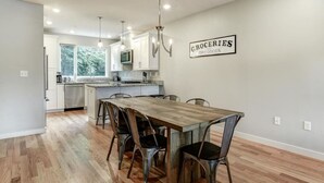 A modern kitchen with a wooden dining table and chairs, a sign reading "GROCERIES AND DRY GOODS", and a view of the outside through the window. - Private Elevator in Hot South Slope (Asheville)