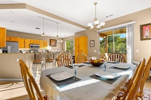 A dining area with a table set for four, a fruit bowl, and a view of the outdoors.