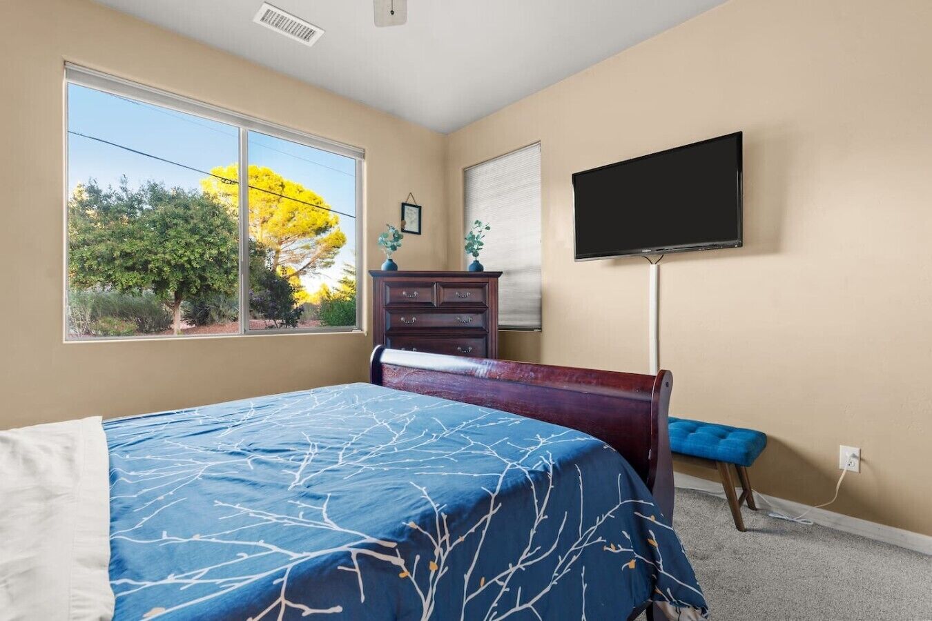 Une chambre à coucher avec un lit, une commode, une télévision et une fenêtre donnant sur des arbres.