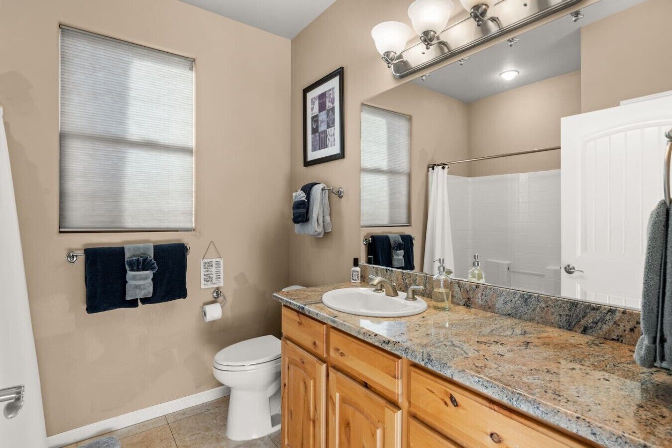 A bathroom with a toilet, sink, vanity, and a large mirror.