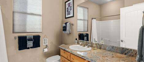 A bathroom with a toilet, sink, vanity, and a large mirror.