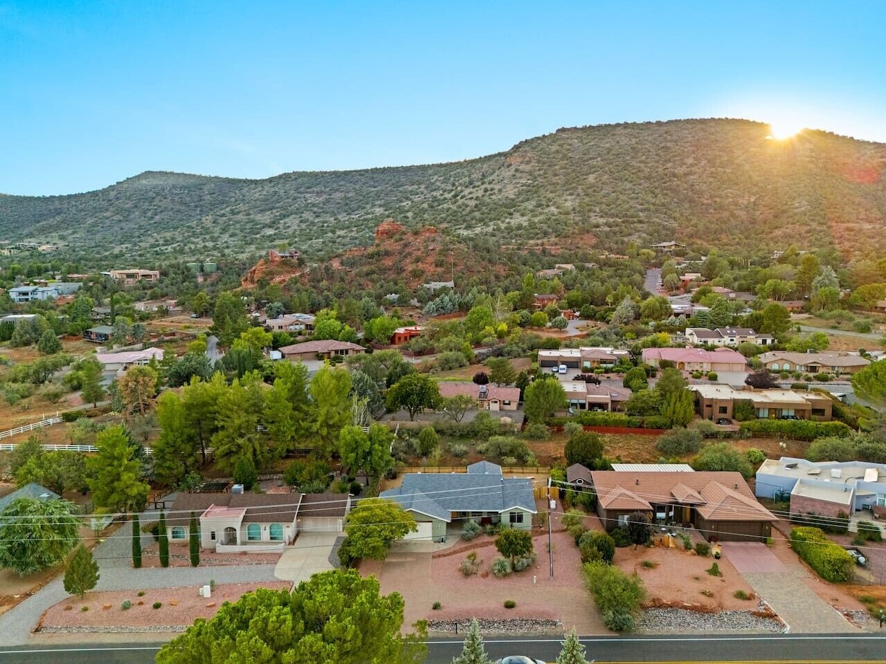 A residential area with houses, trees, and a hilly landscape in the background.