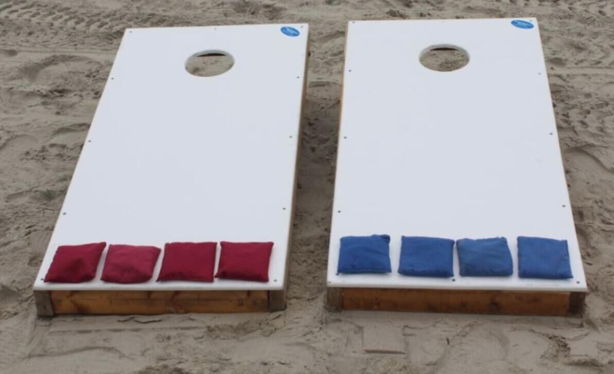 Twee witte rechthoekige objecten met gaten aan de bovenkant en een houten basis, geplaatst op zand.