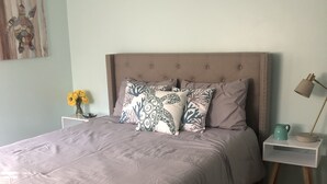 Een slaapkamer met een groot bed, nachtkastje, lamp en een vaas met bloemen.