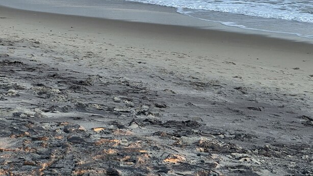 Een strand met golven die op het strand breken, een bewolkte lucht en een verre horizon.