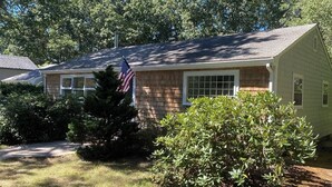 Een gelijkvloers huis met een veranda, een vlag en een verzorgd gazon.