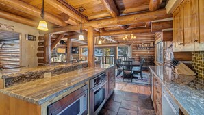 Een interieur van een blokhut met een keuken, voorzien van granieten aanrechtbladen, houten kastjes en een eettafel met stoelen.