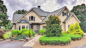 A large, two-story house with a stone facade, a stone entrance, and a well-maintained garden with various plants and a pathway leading to the front door. - Spacious Elk Mountain Sanctuary w/ Deck & Views! (Asheville)