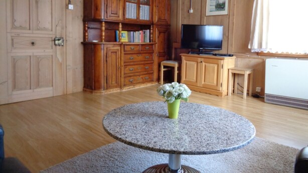A wooden-paneled room with a television, a small table with a vase of flowers, and a large cabinet with drawers.