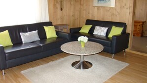 A room with two black sofas, a round table with a vase of flowers, wooden walls, a clock, and a painting.