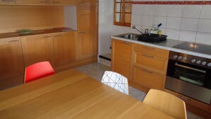 A compact kitchen with wooden cabinets, a dining table, and a red chair.