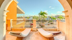 Un balcon avec deux fauteuils de jardin, une vue sur le paysage urbain et un palmier.