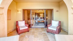 Un espace patio avec deux fauteuils en osier, une porte vitrée donnant sur un coin repas et un ventilateur de plafond.