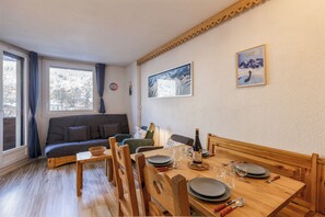 A cozy living room with a sofa, a dining table set for four, and a large window.