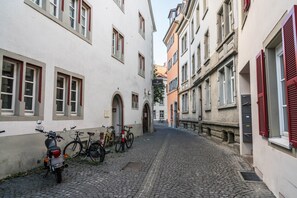 Eine schmale Kopfsteinpflasterstraße gesäumt von Gebäuden, mit einem abgestellten Motorrad und Fahrrädern.