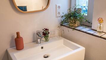 A bathroom with a white sink, a mirror, a potted plant, and a vase with flowers.