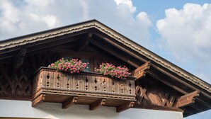 Ein Holzbalkon mit Blumen, Teil eines Gebäudes mit geneigtem Dach und Holzbalken.