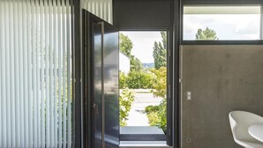 A modern interior with a sliding glass door leading to a garden, a white chair, and a concrete wall.