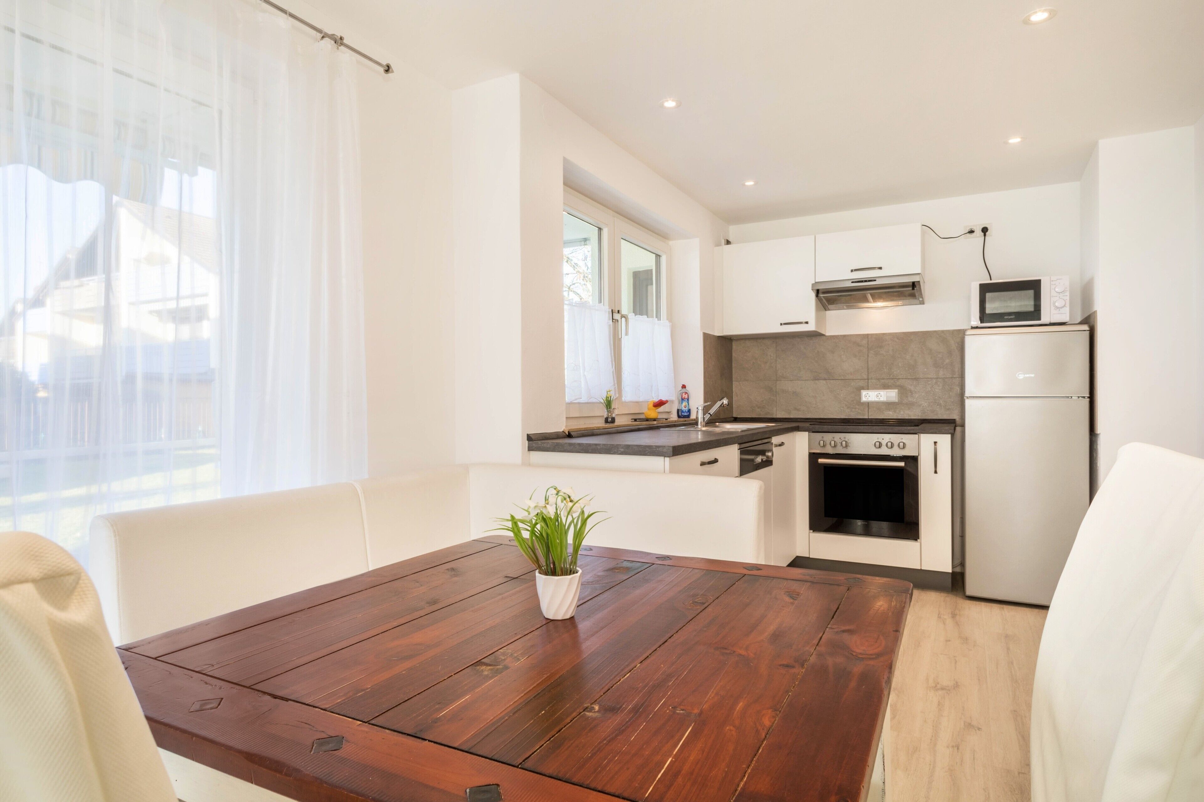 A modern kitchen with white cabinetry, a wooden dining table, and a potted plant.