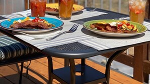 A table with breakfast plates and iced drinks on a deck with a mountain view in the background. - Ark Valley BV Home New Construction STR-108 (Buena Vista)