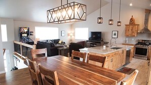 A modern kitchen with wooden cabinets, a large island, and a dining area with a wooden table and chairs. - Ark Valley BV Home New Construction STR-108 (Buena Vista)