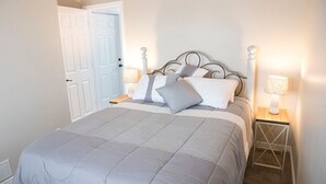 A bedroom with a bed, two bedside tables with lamps, a door, and a carpeted floor. - Ark Valley BV Home New Construction STR-108 (Buena Vista)