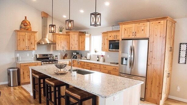 A modern kitchen with wooden cabinets, a stainless steel refrigerator, and a granite countertop. - Ark Valley BV Home New Construction STR-108 (Buena Vista)