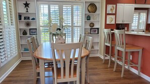 Un coin repas avec une table et des chaises en bois, un vase décoratif avec des fleurs et un mur avec des étagères contenant divers objets, ainsi qu'une pancarte indiquant « RELAX ».