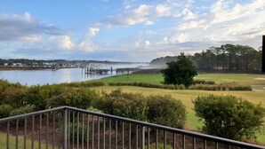 Une vue depuis un balcon donnant sur un terrain de golf, un plan d’eau et une ville située au loin.