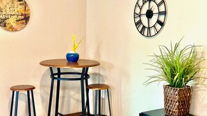 A room with a round table, two stools, a clock, a decorative sign, and a potted plant. - Upper Mesa Villa #1, Glacier Suites - Upper Mesa Villa #1 (Matanuska-Susitna)