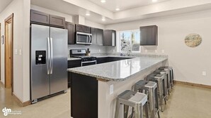 A modern kitchen with a central island, stainless steel appliances, and bar stools. - Upper Mesa Villa #1, Glacier Suites - Upper Mesa Villa #1 (Matanuska-Susitna)