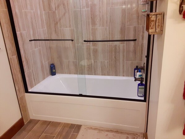 Una ducha a nivel con puerta de cristal, paredes de azulejos y una bañera blanca.