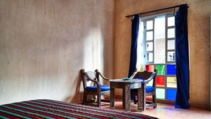 A room with a bed, two chairs, a small table, and a window with blue curtains. - Bienvenue au Riad Taroudant ! (Taroudant)
