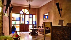 A room with a checkered floor, a round table, a chair, and a large window with stained glass. - Bienvenue au Riad Taroudant ! (Taroudant)