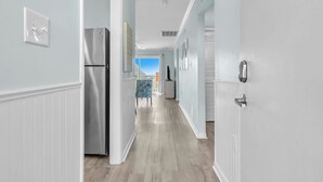 Un pasillo con un refrigerador, una mesa de comedor con sillas y vista al cielo.