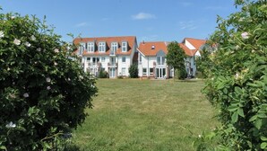 A row of white buildings with red roofs, surrounded by green lawns and bushes. - Sünnslag Whg. Sü5/118 (Ostseebad Boltenhagen)