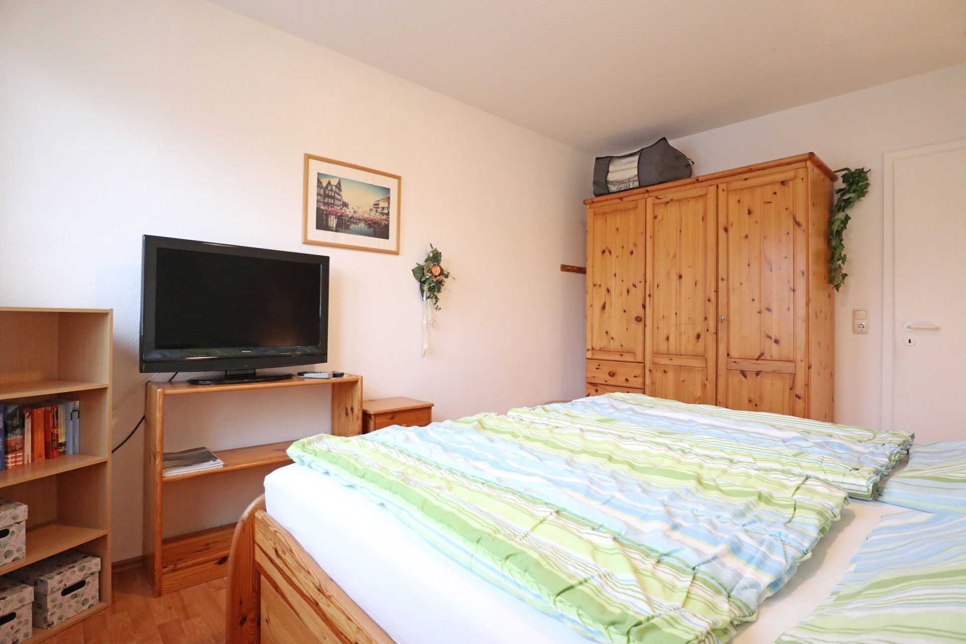 Ein Schlafzimmer mit einem Bett, einem Fernseher auf einem Holzständer, einem Holzschrank und einer kleinen Bücherablage.