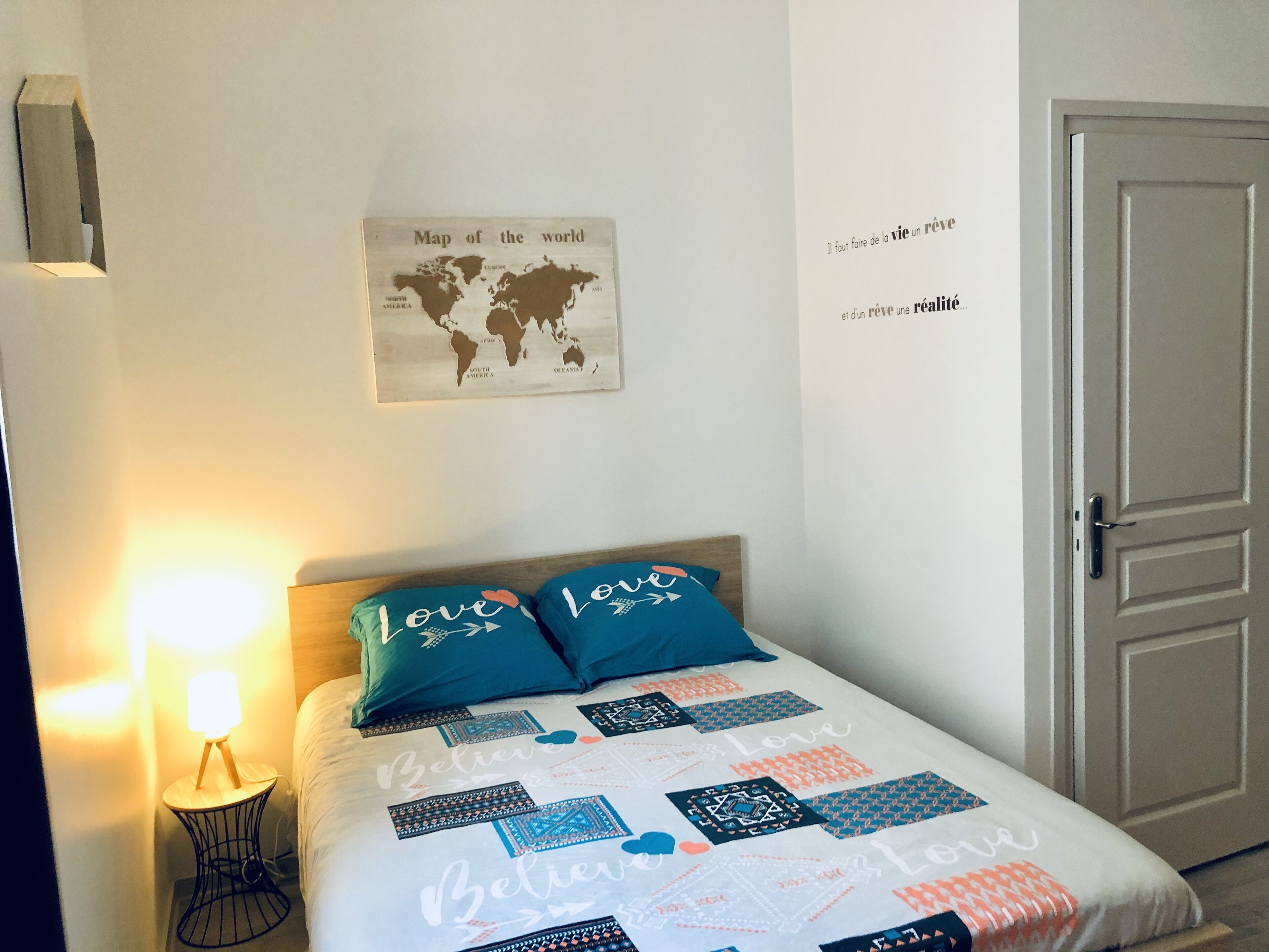 Ein Schlafzimmer mit einem Bett, einer Weltkarte und einem Zitat an der Wand.