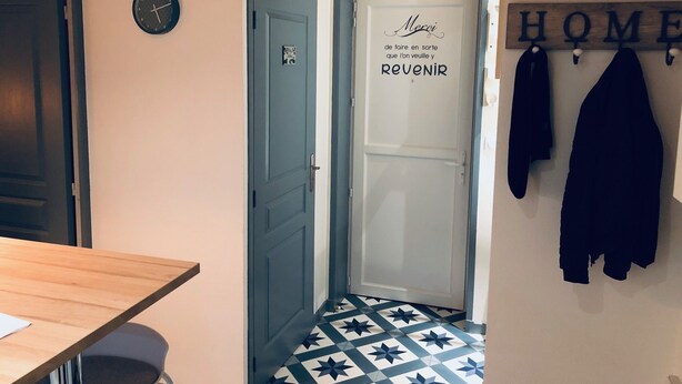 En hall med en dörr där det står "Var vänlig att se till att folk vill komma och KOMMA TILLBAKA" och en klädställning med jackor.