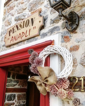 Un bâtiment en pierre avec une enseigne en bois indiquant « PENSION ANAPLI » et le numéro « 21 » sur la porte.