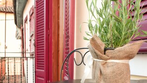 A metal table with a burlap-wrapped plant on it, set on a wooden deck with red shutters in the background.